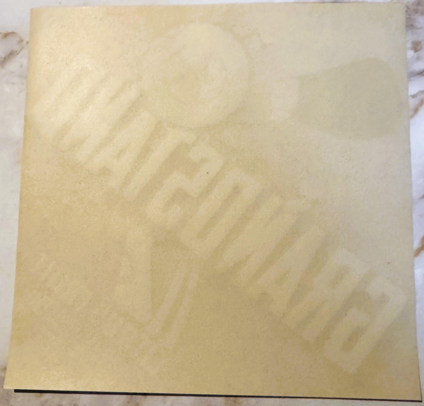 Cream-colored vintage citrus crate label with faint embossed design, photographed flat on marble surface
