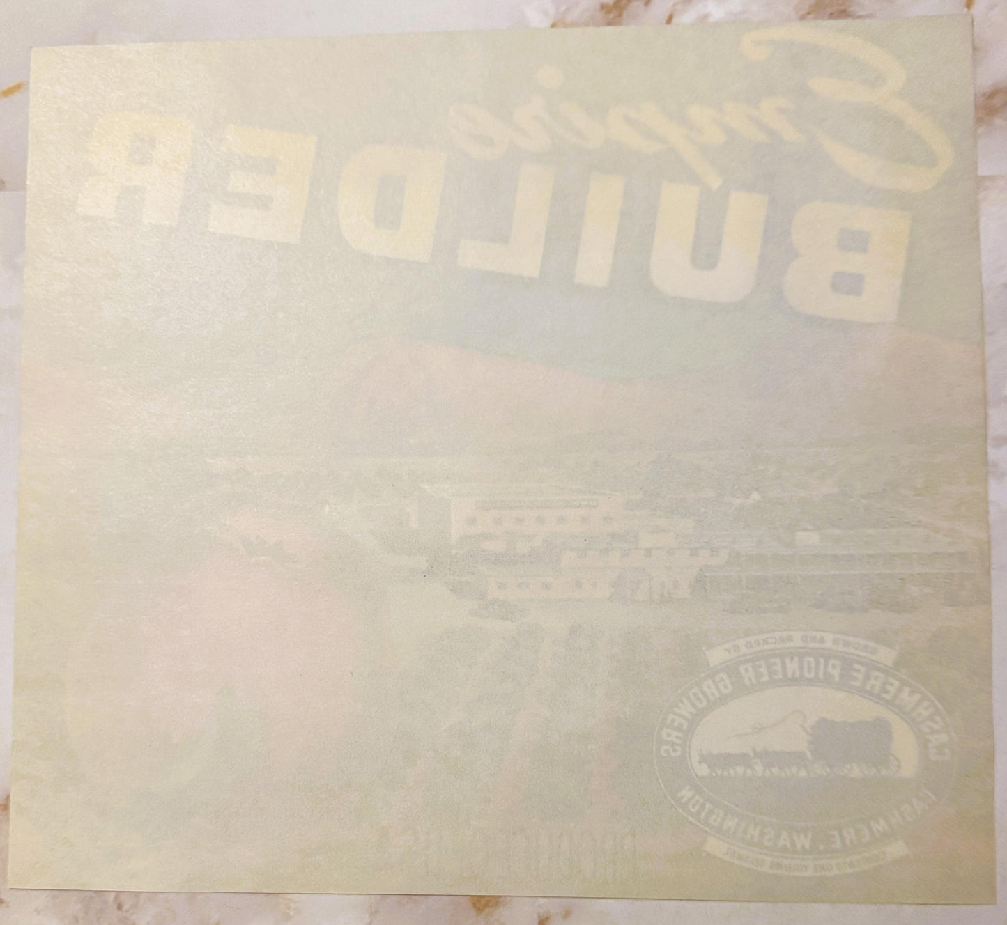 Cream-colored vintage apple crate label with "Empire Builder" text and railroad logo, photographed flat on marble surface