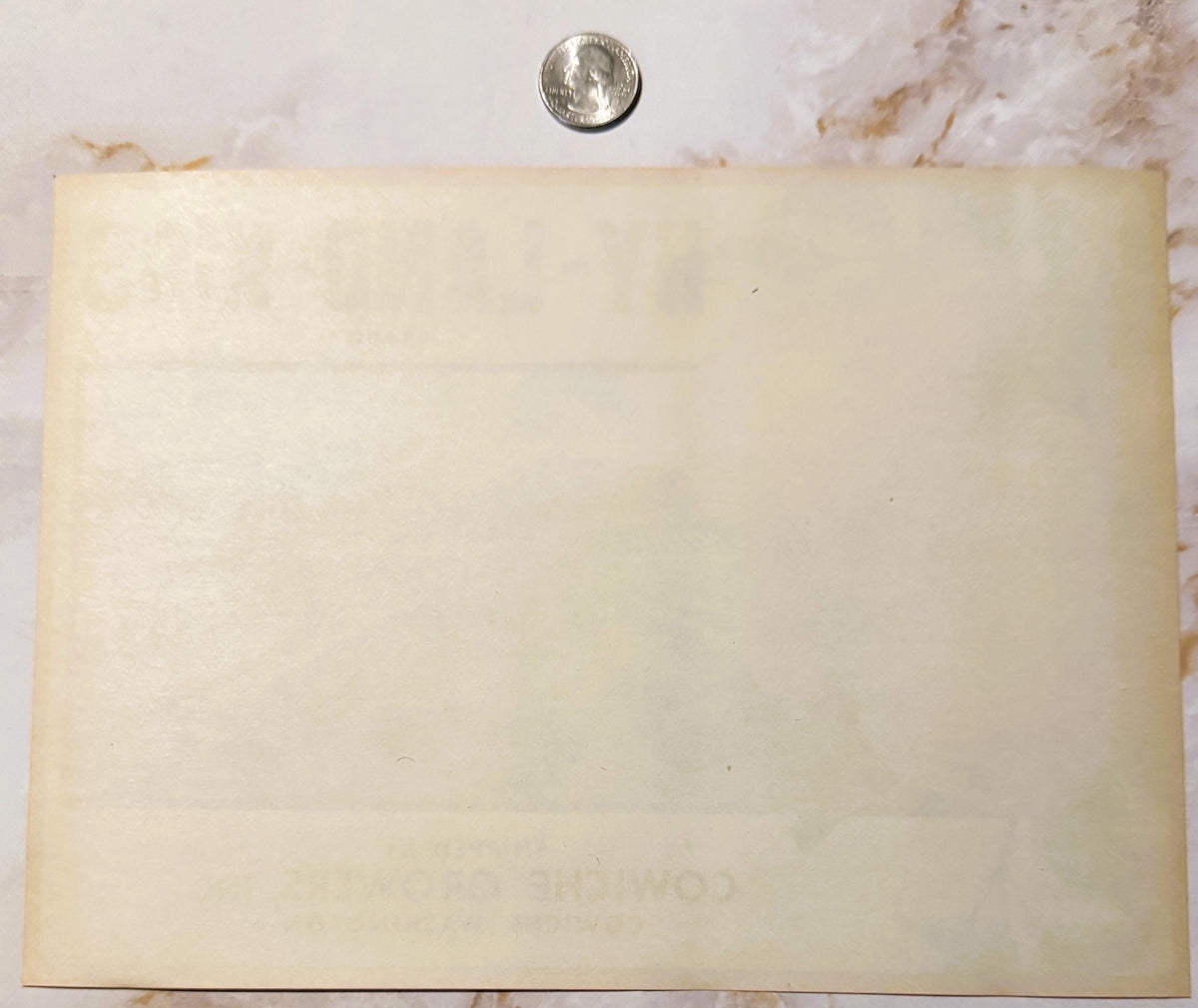 Cream-colored vintage fruit label next to quarter for scale, showing faded printing and aged paper with stains