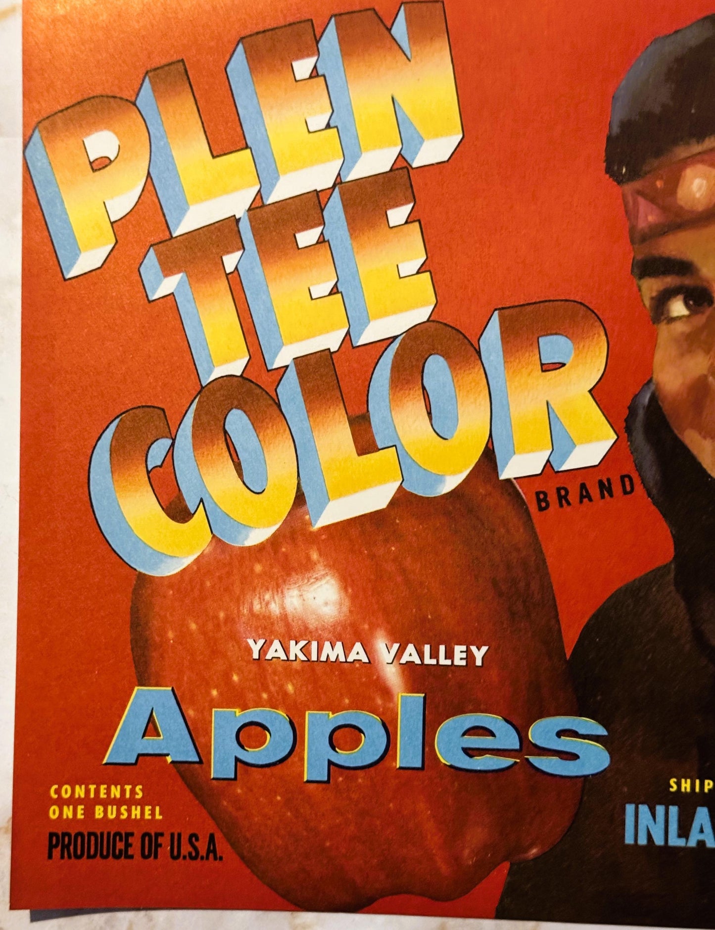 Vintage Plen Tee Color Brand apple crate label featuring bold 3D lettering and a large red apple on orange background, held b