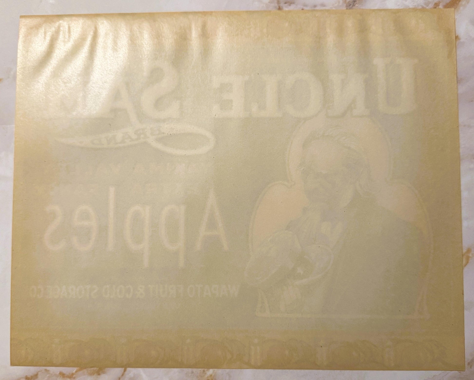 Faded cream-colored crate label with embossed text reading "Uncle Sam" and "Yakima" among other barely visible wording, photo