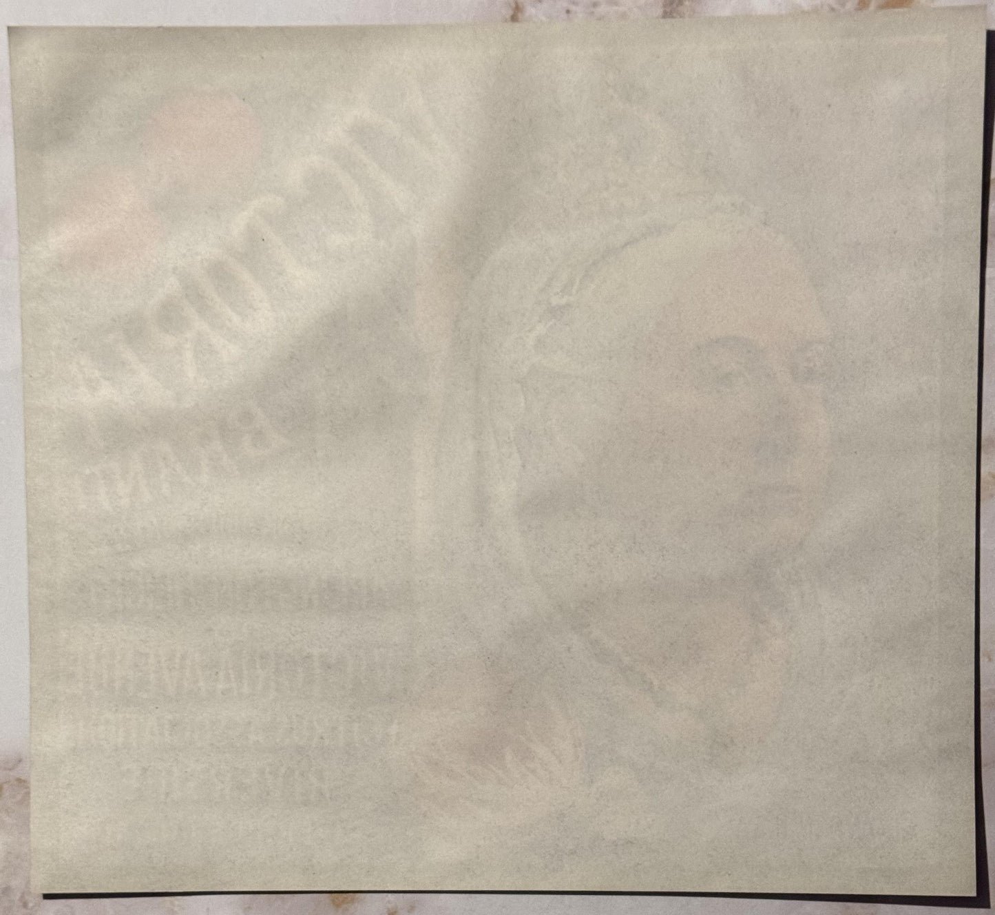 Faded vintage crate label on cream paper with embossed text, showing wear and age spots, photographed flat against a light ba