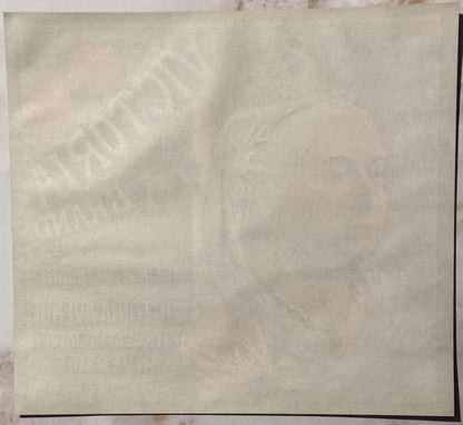 Faded vintage crate label on cream paper with embossed text, showing wear and age spots, photographed flat against a light ba