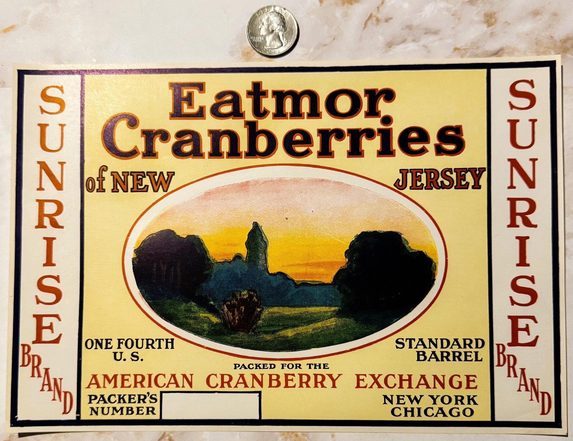 Vintage cranberry barrel label from Eatmor of New Jersey with landscape illustration, quarter coin for scale at top.