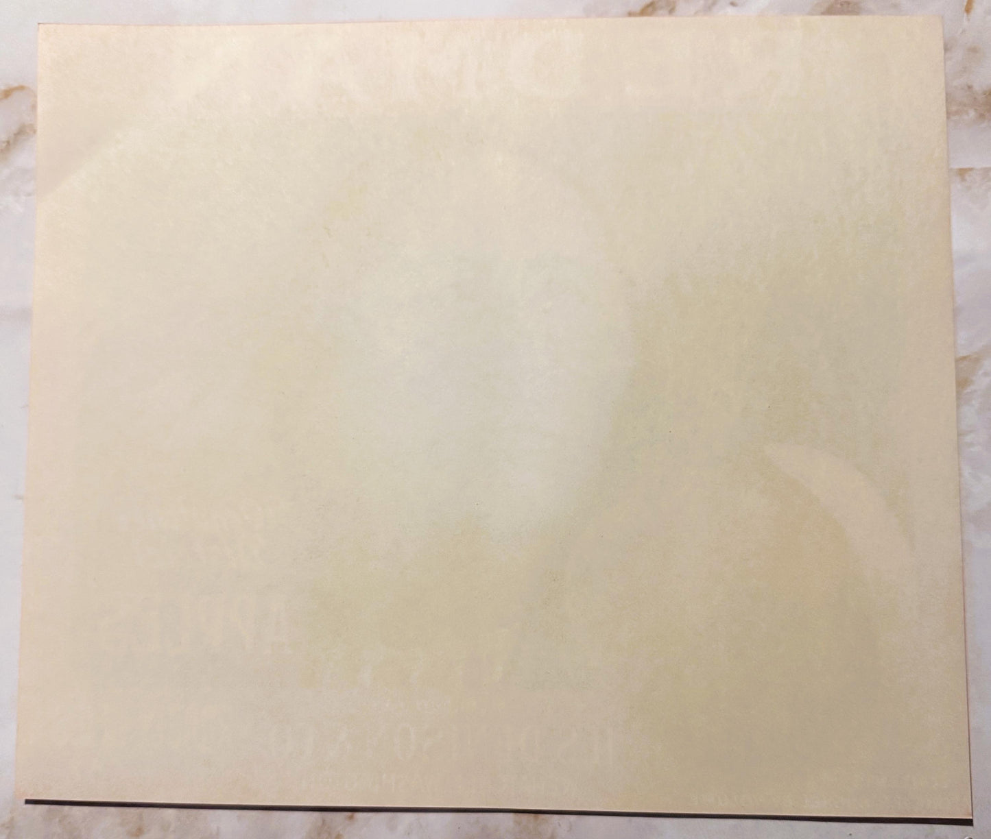 Blank cream-colored vintage apple crate label on marble surface with dark line at bottom edge