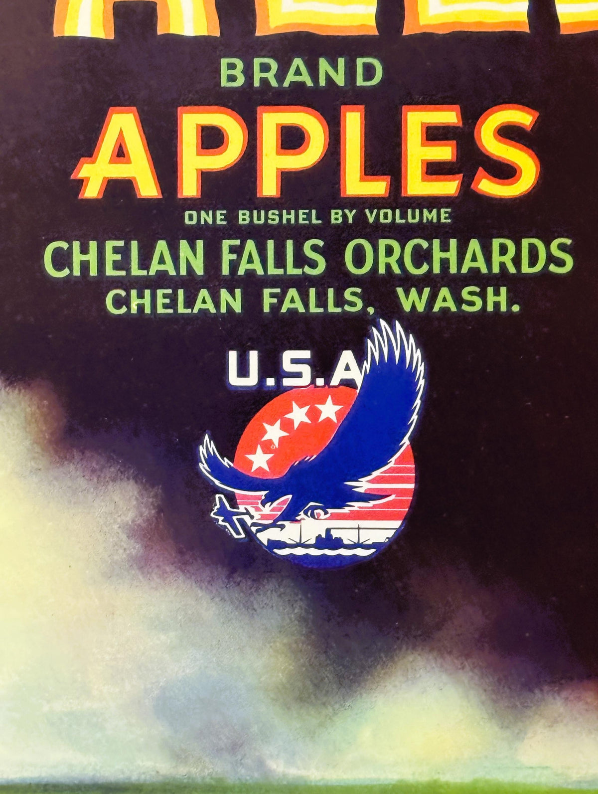 Vintage apple crate label with yellow and red "APPLES" text, eagle logo, and Chelan Falls Orchards branding on dark backgroun
