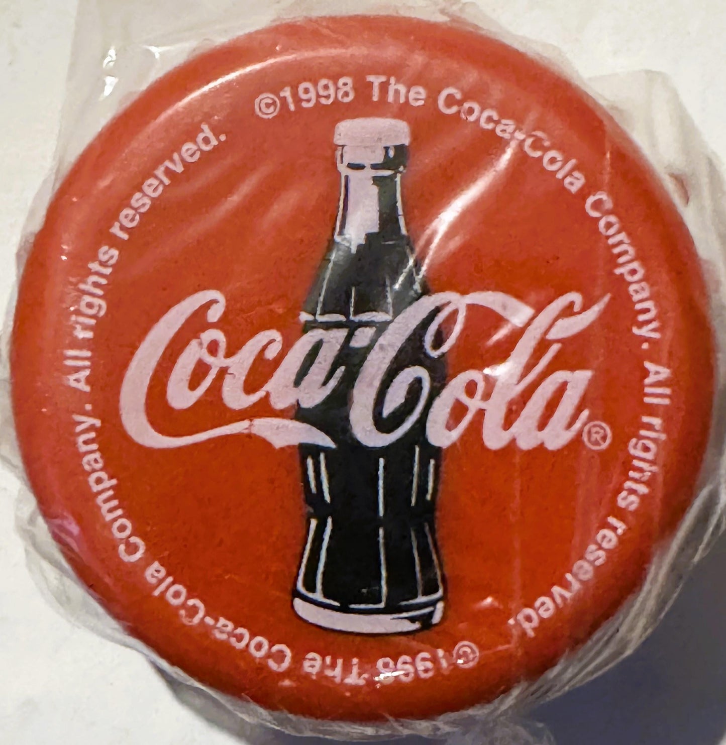 Red circular yo-yo with Coca-Cola branding, bottle image, and copyright text, still sealed in clear plastic packaging