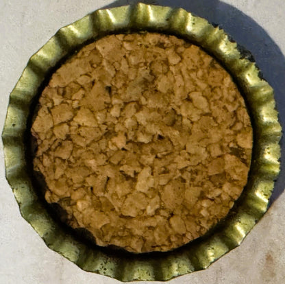 Overhead view of a vintage bottle cap with ridged metal rim and cork-lined tan interior against light background