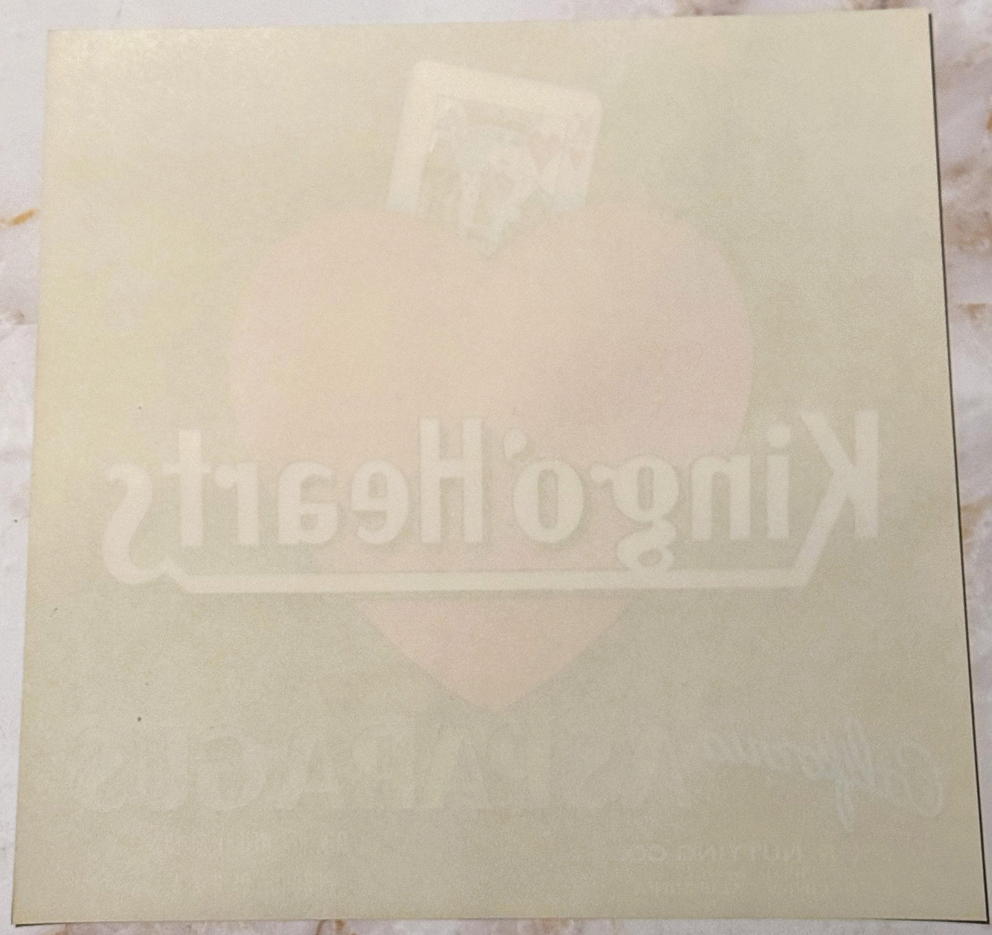 Cream-colored vintage crate label with faint embossed King of Hearts design and text, photographed flat against white backgro
