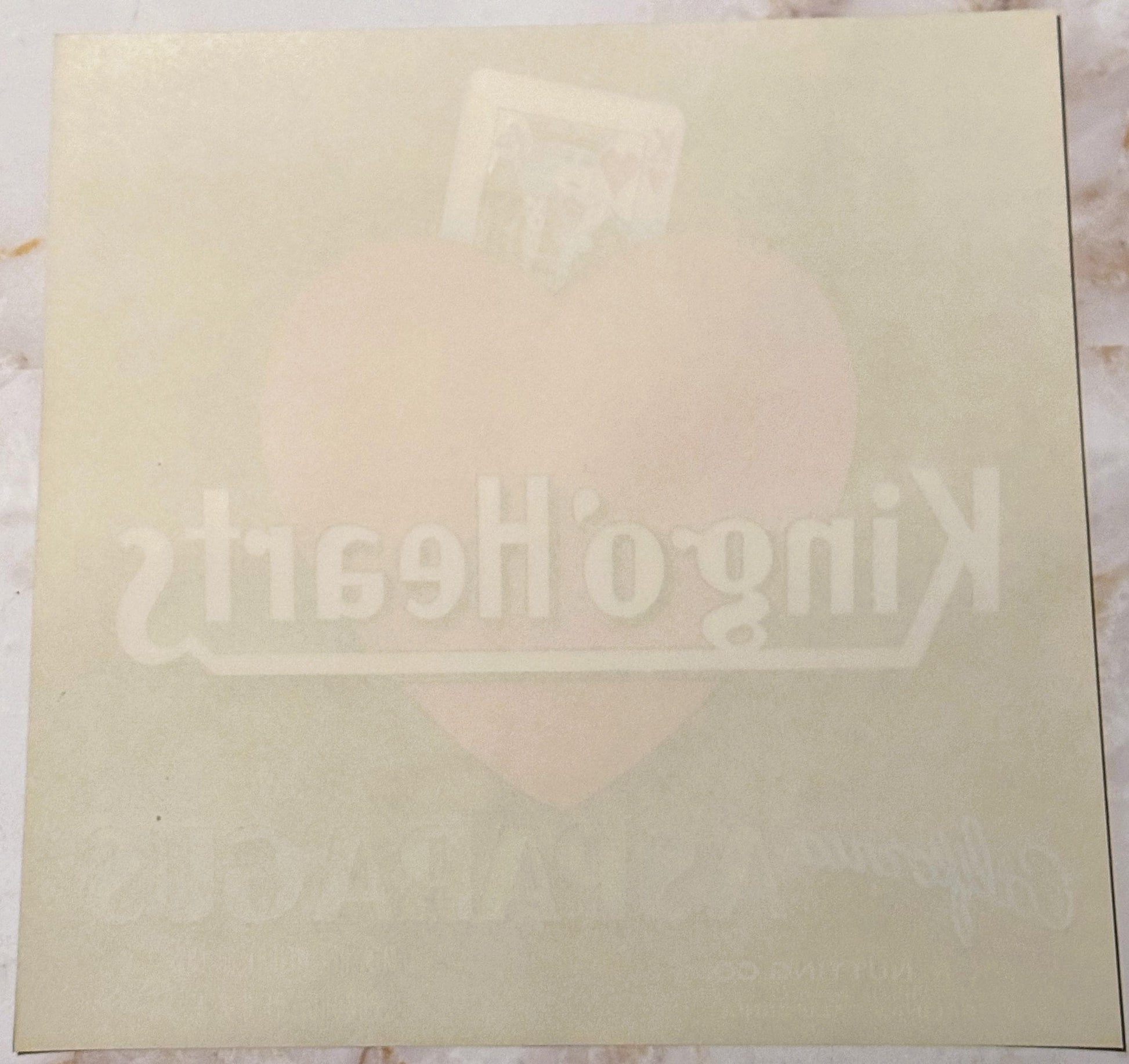 Cream-colored vintage crate label with faint embossed King of Hearts design and text, photographed flat against white backgro