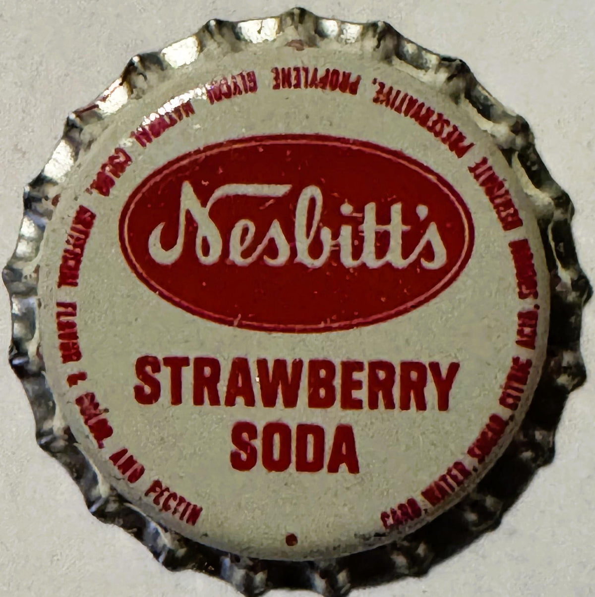 Vintage Nesbitt's Strawberry Soda bottle cap with red and cream colors, shown flat against gray background