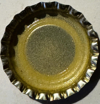 Vintage bottle cap with corrugated metal rim, yellow and tan concentric circles, tan center with embossed text, viewed from a