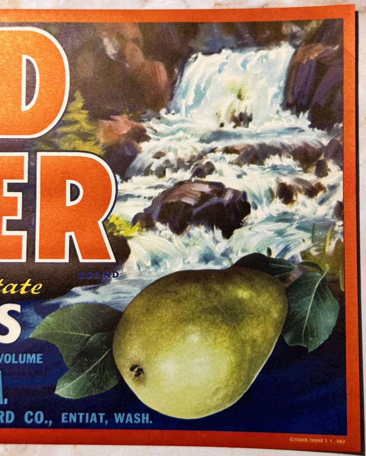 Vintage fruit crate label with orange border showing a pear and waterfall scene, partial text "D" and "ER" visible, printed b