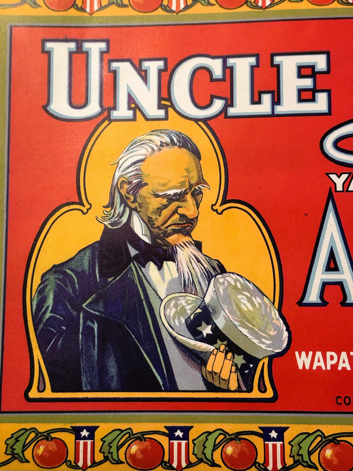 Vintage Uncle Sam apple crate label with bearded man in formal attire holding a hat against red and gold background with deco