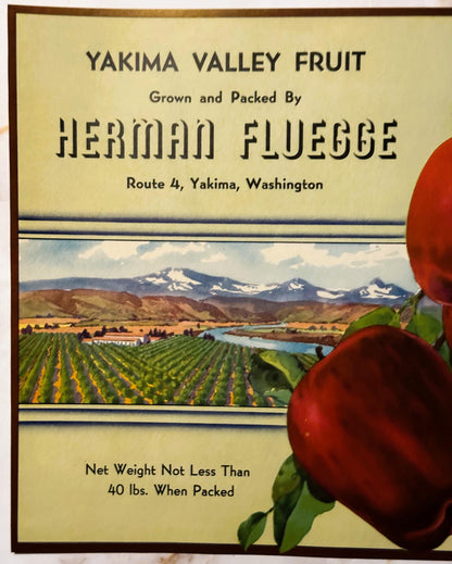 Vintage fruit crate label for Yakima Valley apples by Herman Fluegge, featuring mountain landscape and red apples on the righ