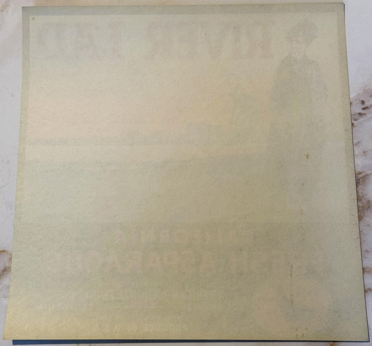 Blank cream-colored vintage crate label with dark blue stripe at bottom, photographed flat on speckled surface