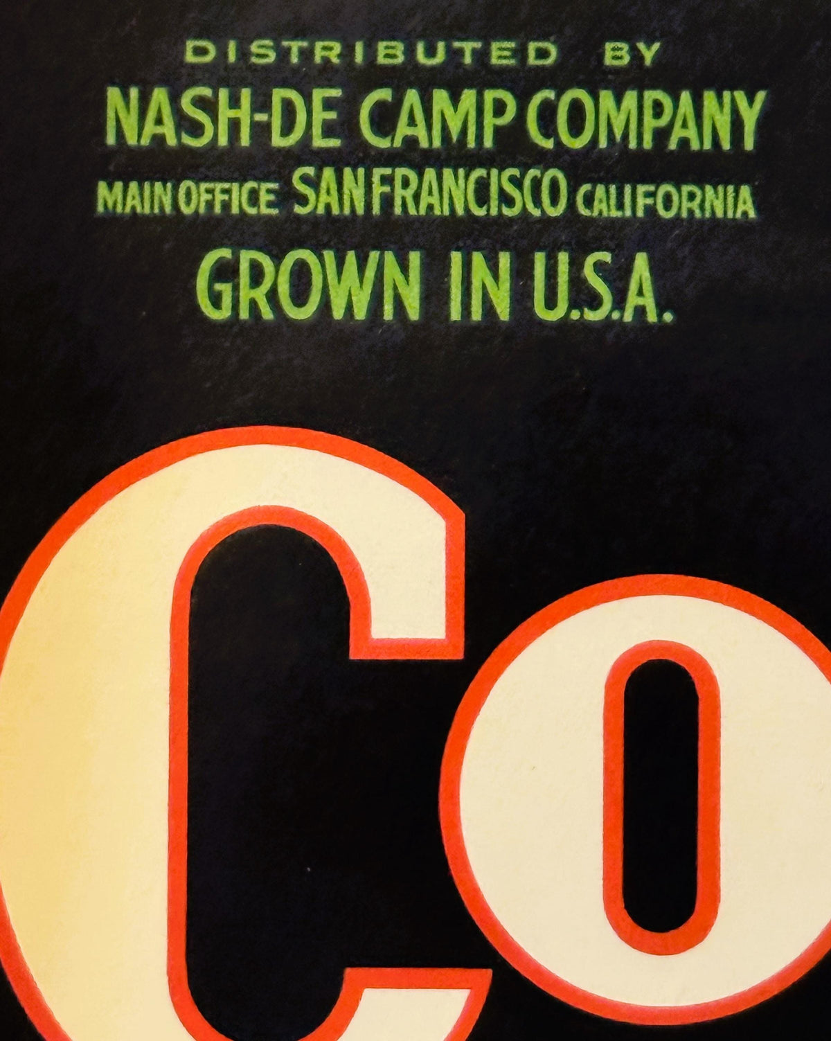 Vintage crate label with lime green text on black background and large red-outlined letters reading "CO" at bottom, distribut