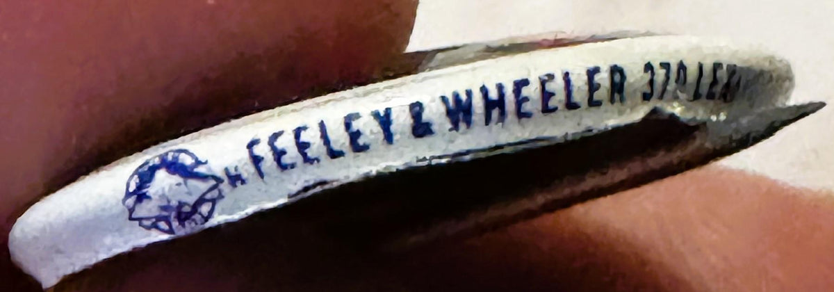 Vintage campaign pin with blue text reading "H. FEELEY & WHEELER 370 ILLIN" on white background, held in hand for scale