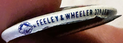 Vintage campaign pin with blue text reading "H. FEELEY & WHEELER 370 ILLIN" on white background, held in hand for scale
