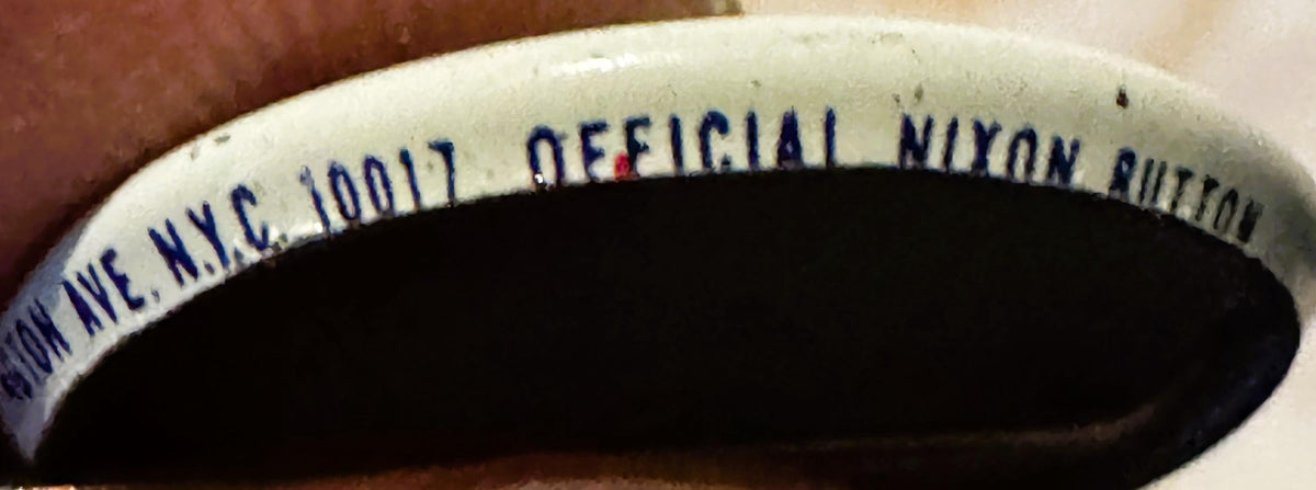 Close-up of a vintage political campaign button rim showing blue text reading "OFFICIAL NIXON BUTTON" on cream-colored materi