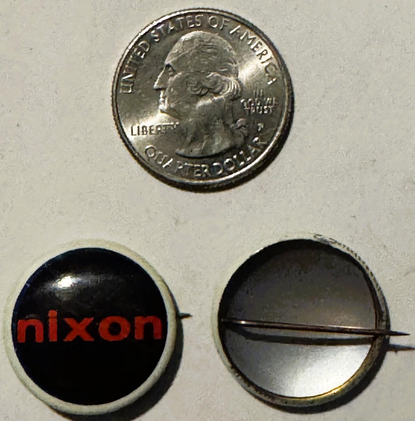 Vintage Nixon campaign button with red text on black background, shown next to a quarter for scale, displaying front and back