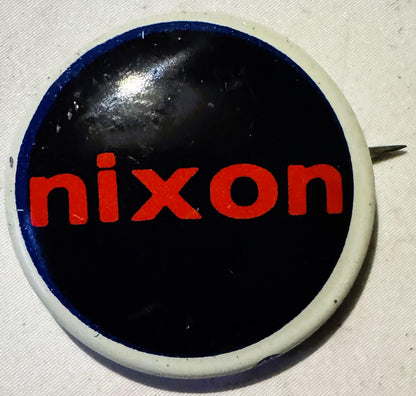 Round campaign button, blue rim, cream ground, dark centre panel with red "nixon" lettering