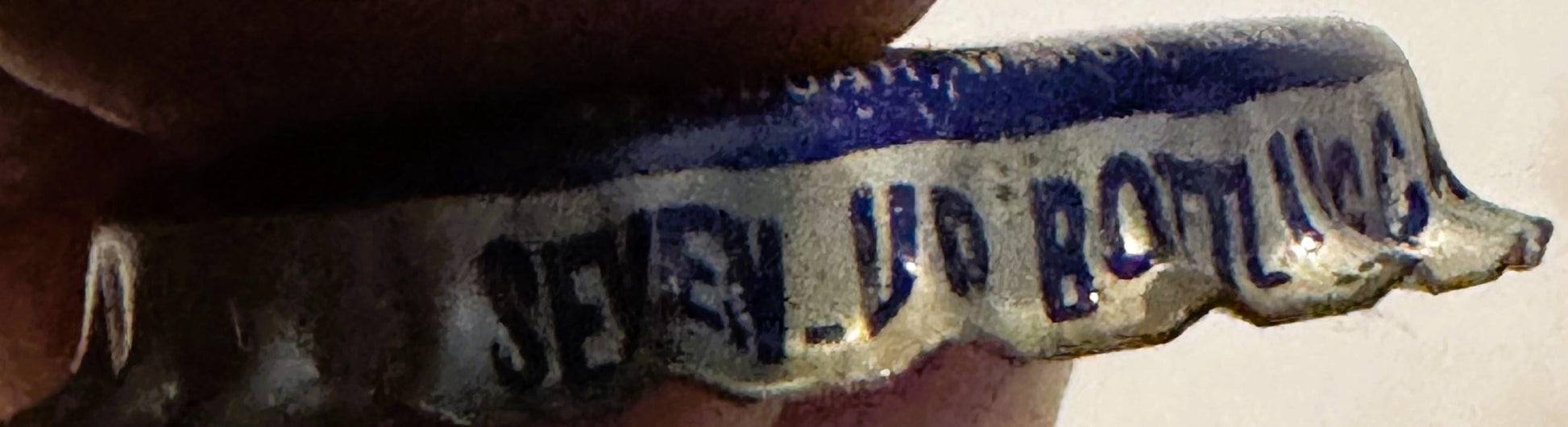 Close-up of vintage cream soda bottle cap with blue top and cream-colored ribbed sides, held in hand, showing embossed text i