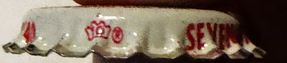 Vintage bottle cap with cream and red coloring, showing crown design and partial text reading "SEVEN" and other faded letteri