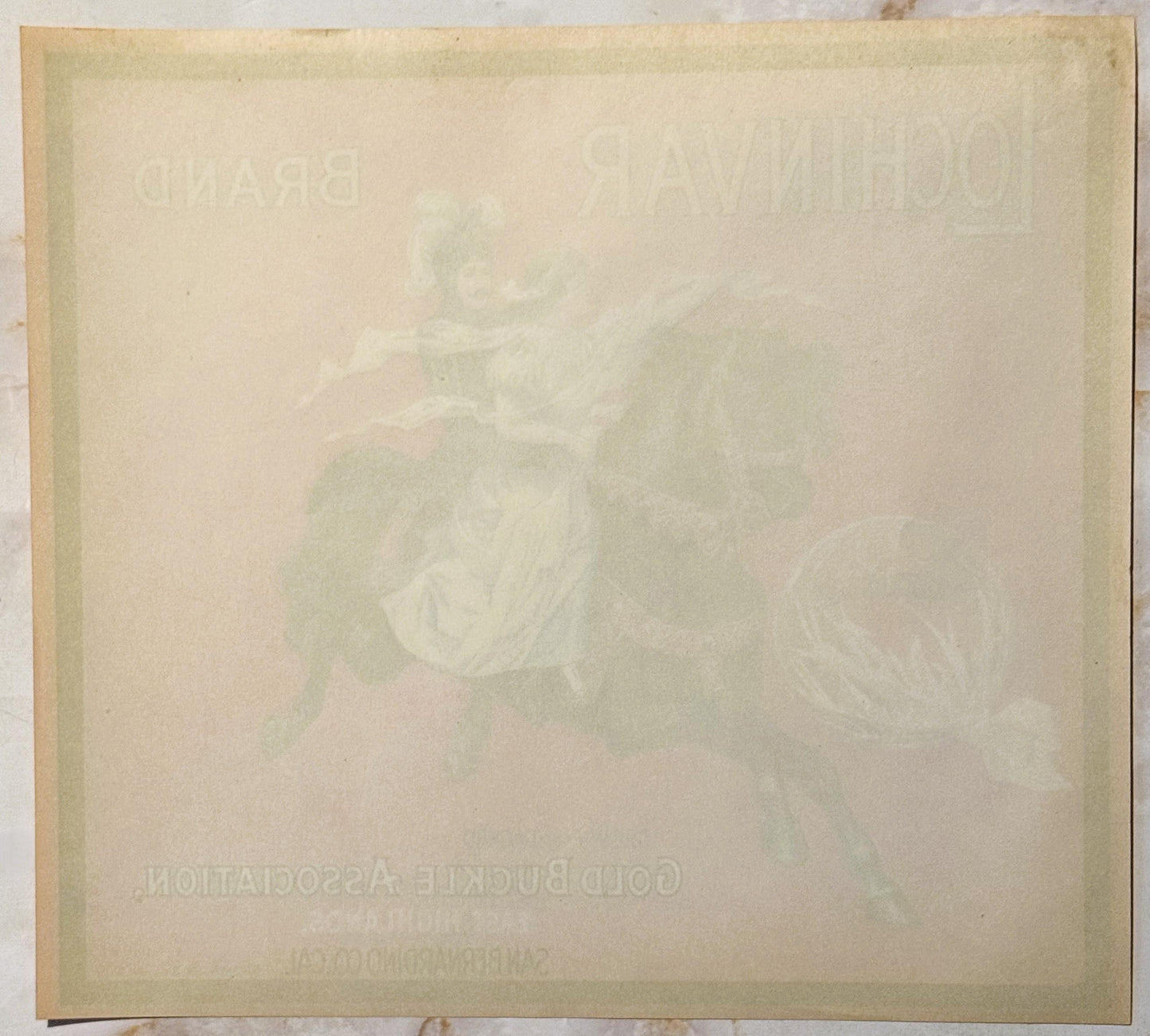Aged cream-colored crate label with faint embossed or printed imagery and text, laid flat showing wear and discoloration