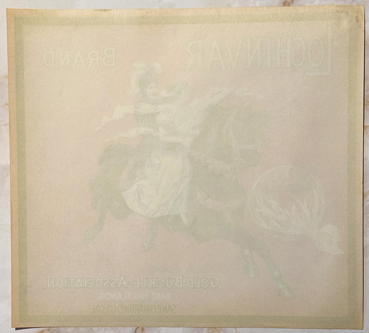 Aged cream-colored crate label with faint embossed or printed imagery and text, laid flat showing wear and discoloration
