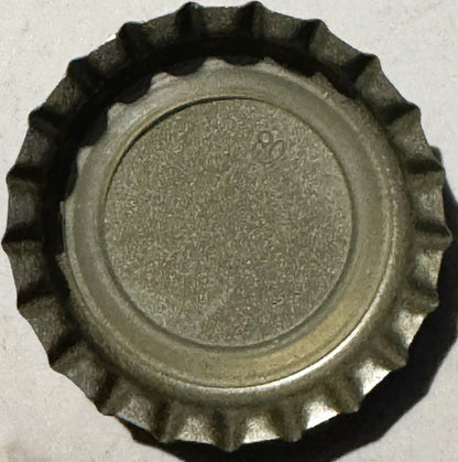 Vintage metal bottle cap with fluted crown edges and textured center, viewed from above against white background