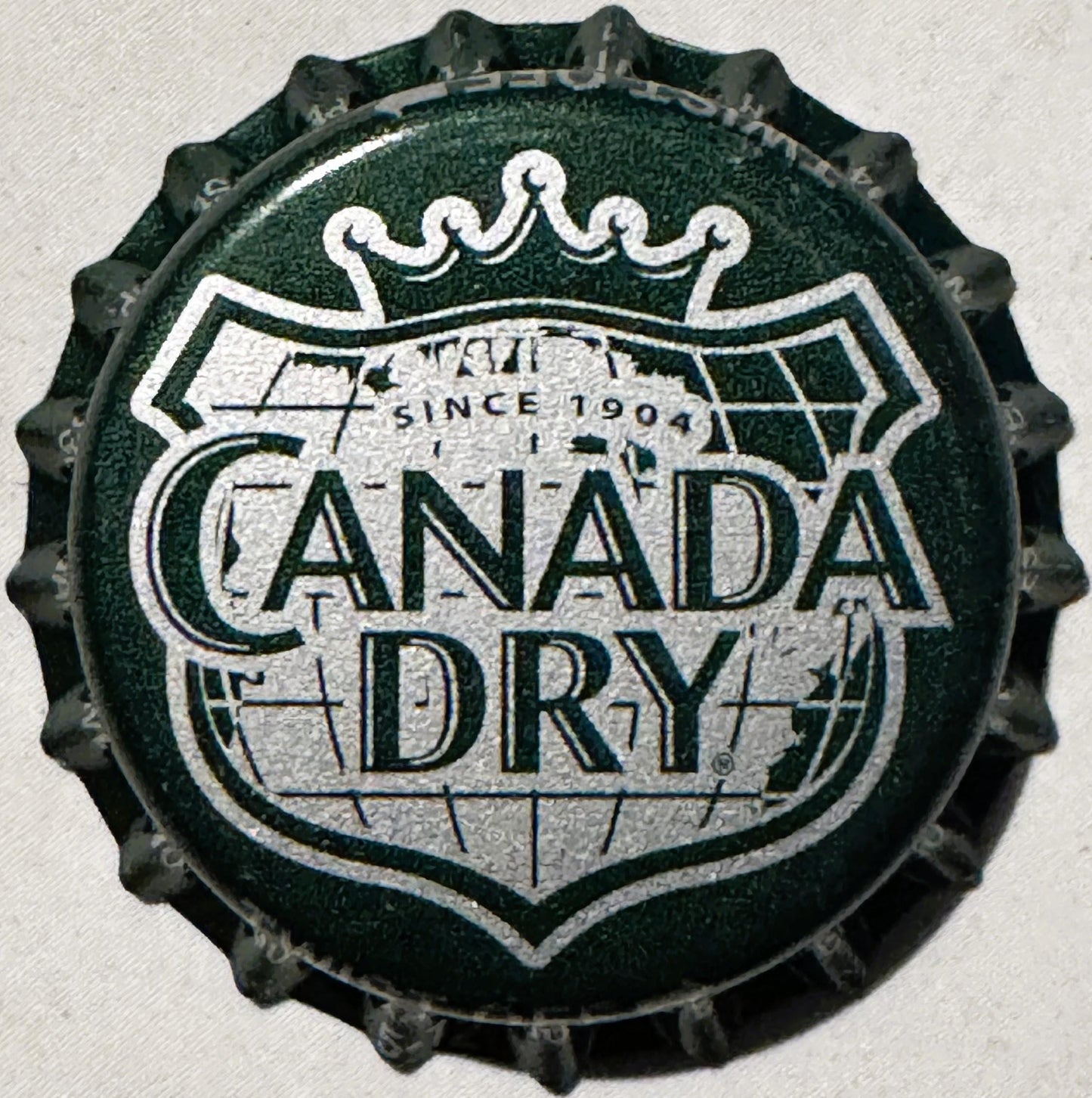 Vintage bottle cap with green and silver crown logo embossed with "Canada Dry" text and "Since 1904" on white background, sho