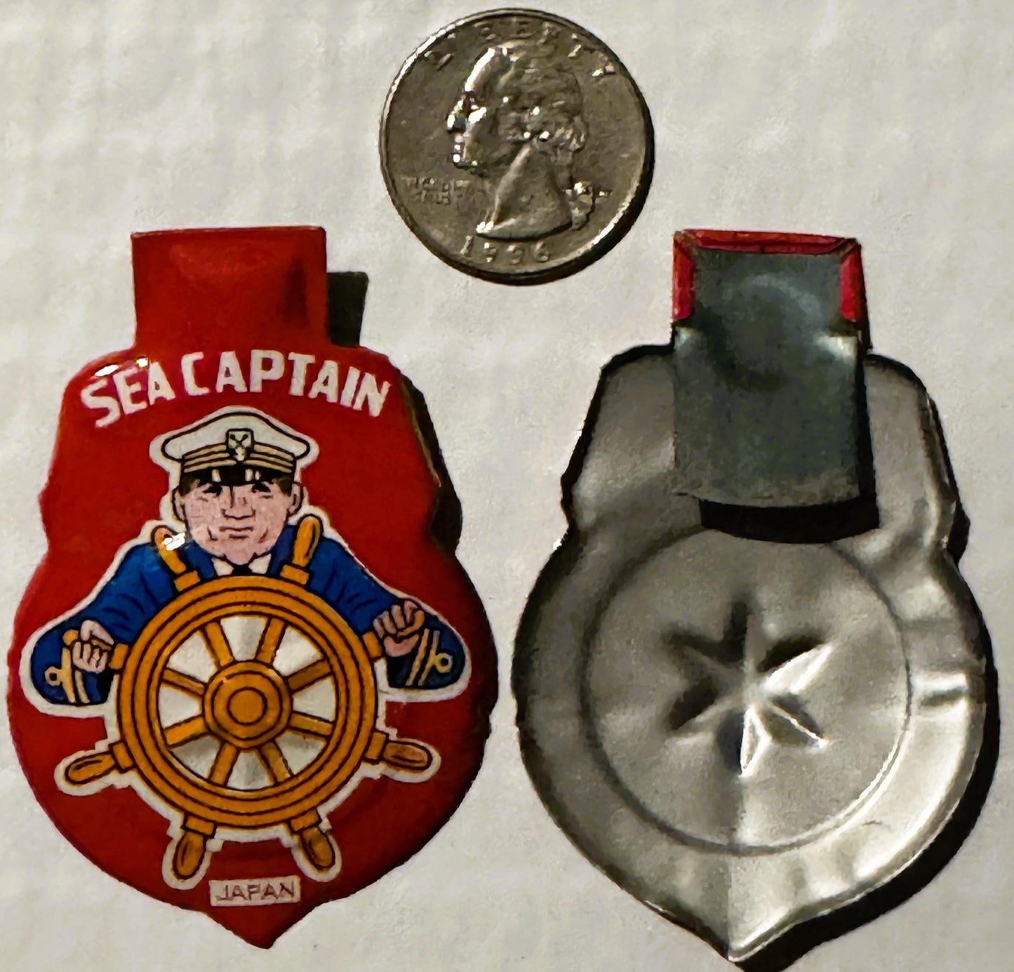Vintage tin litho clicker toy showing red "Sea Captain" front with sailor at ship wheel and silver metal back, scaled with qu