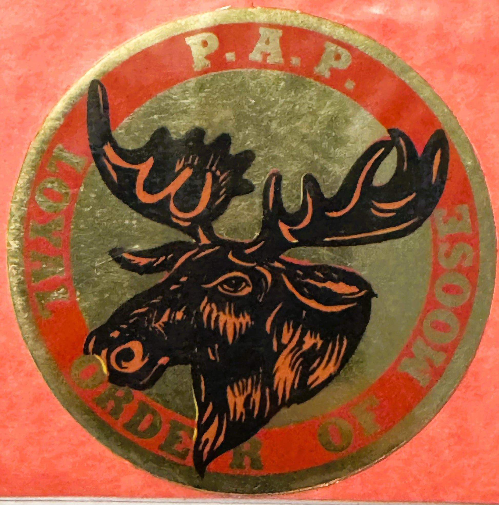 Circular emblem with black moose head outlined in orange on gray center, surrounded by red band with "R.A.P." at top and "LOY