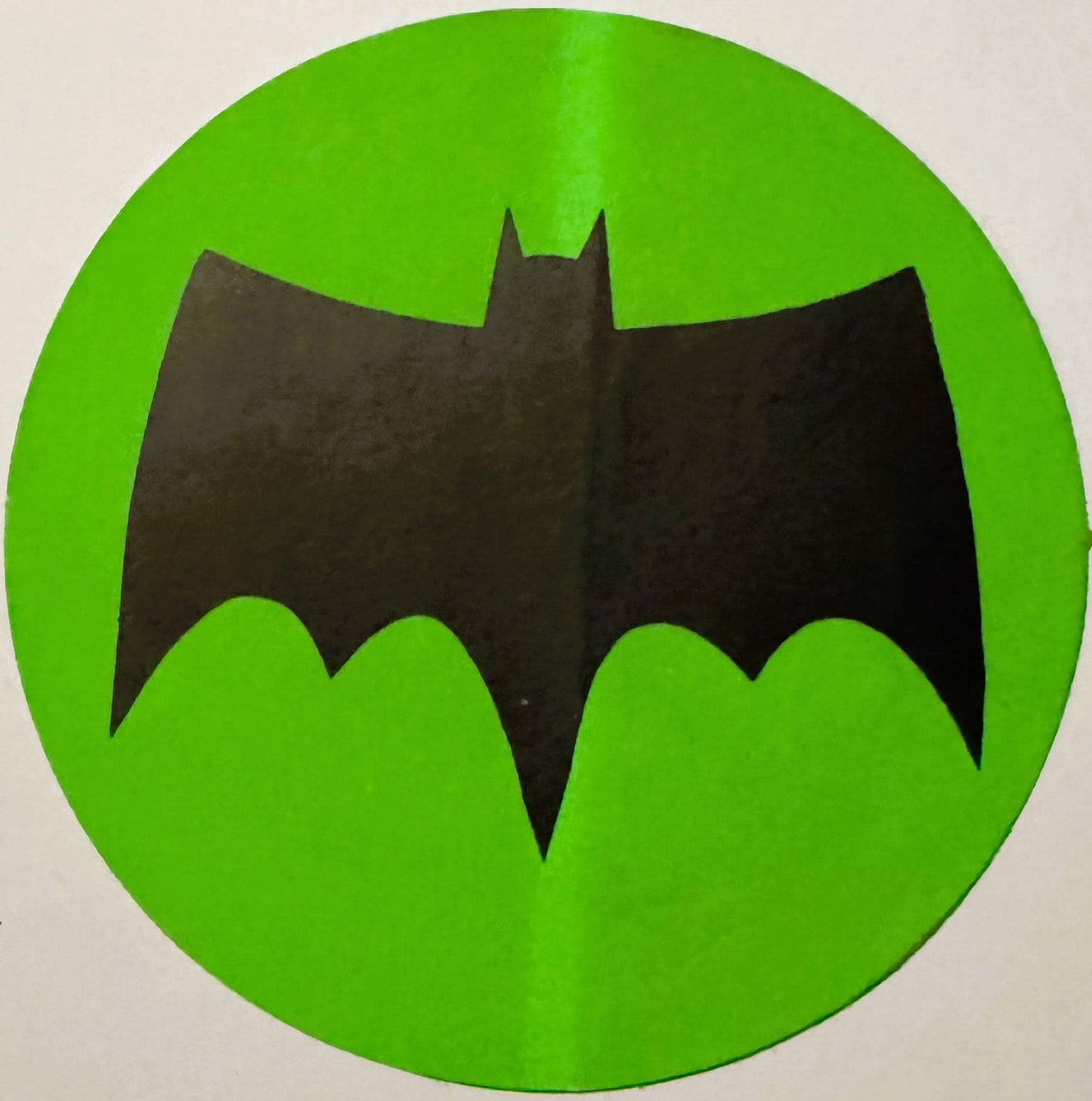 Black bat symbol on bright green circular sticker or decal, vintage 1960s Batman Signal design