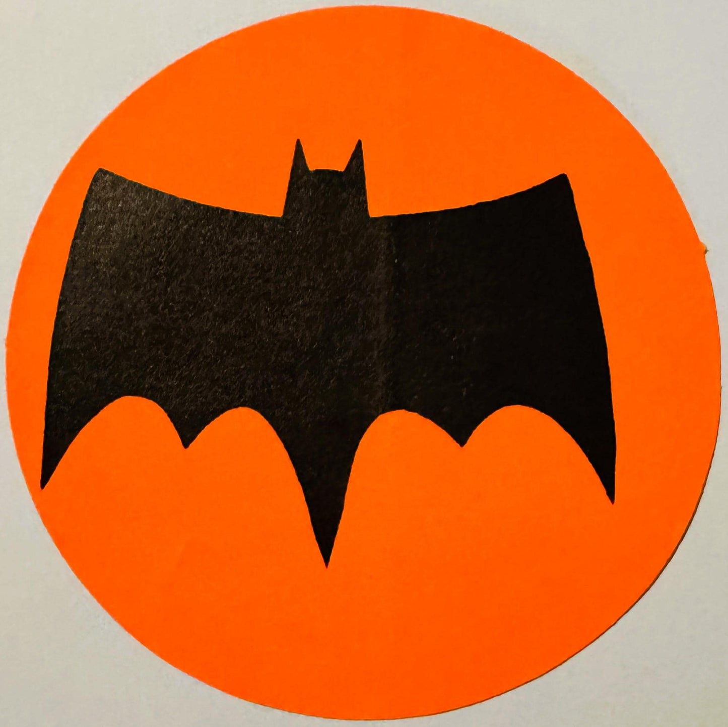 Black bat silhouette on bright orange circular background, vintage sticker or decal with pointed ears and wings