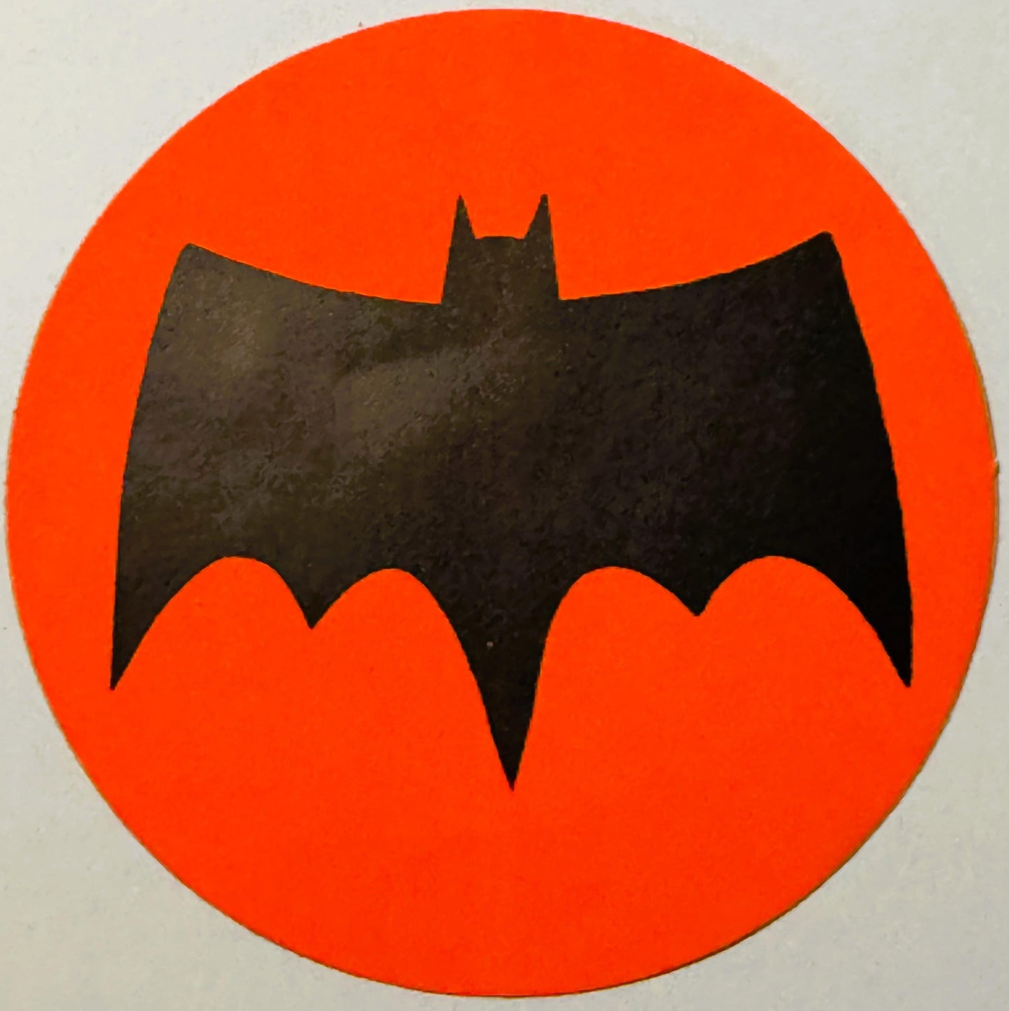 Black bat silhouette on bright red-orange circular background, vintage sticker with textured surface