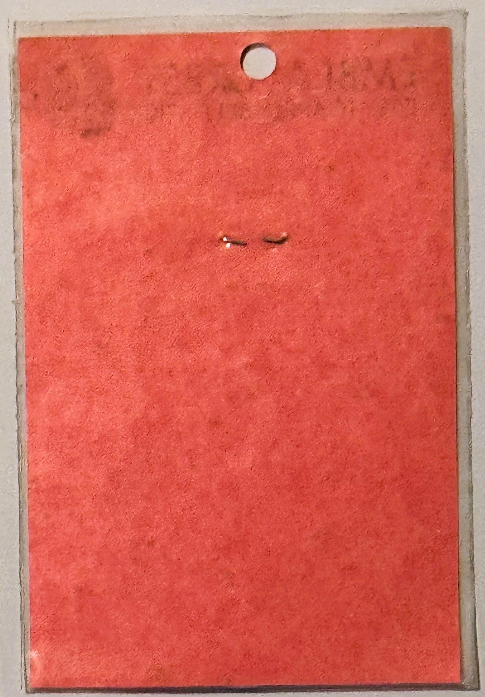 Red vintage decal card with circular hole at top and two small embossed marks in center, displayed against clear backing