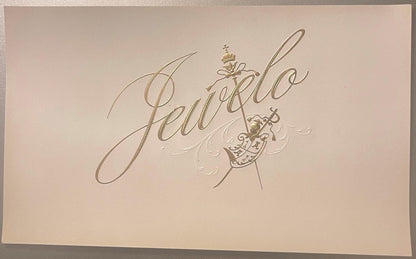 Gold embossed cigar label on cream cardstock reading "Jewelo" in flowing script with decorative coat of arms and ornamental f
