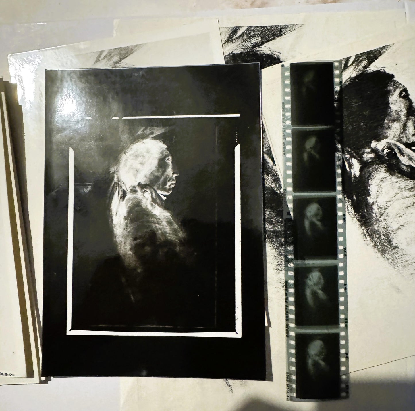 Black and white charcoal portrait print mounted on black matting, displayed with film strip negatives and reference materials
