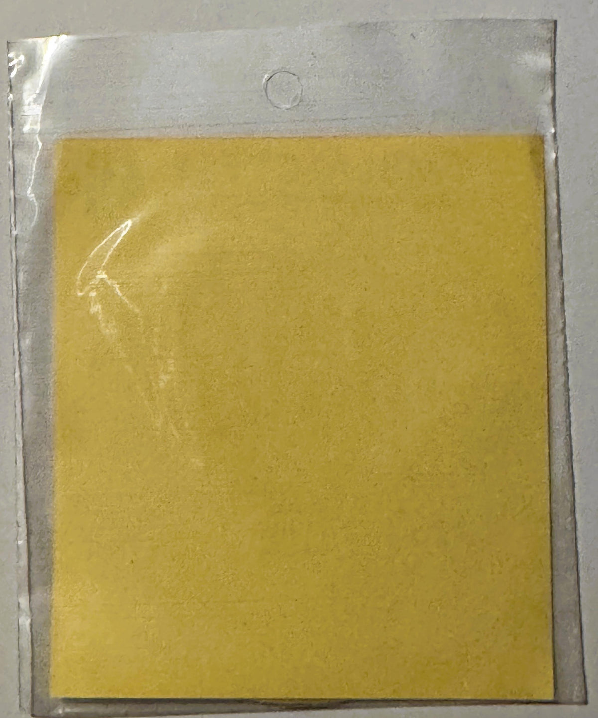Vintage yellow decal sticker in clear plastic sleeve with hanging hole, plain surface visible from front angle