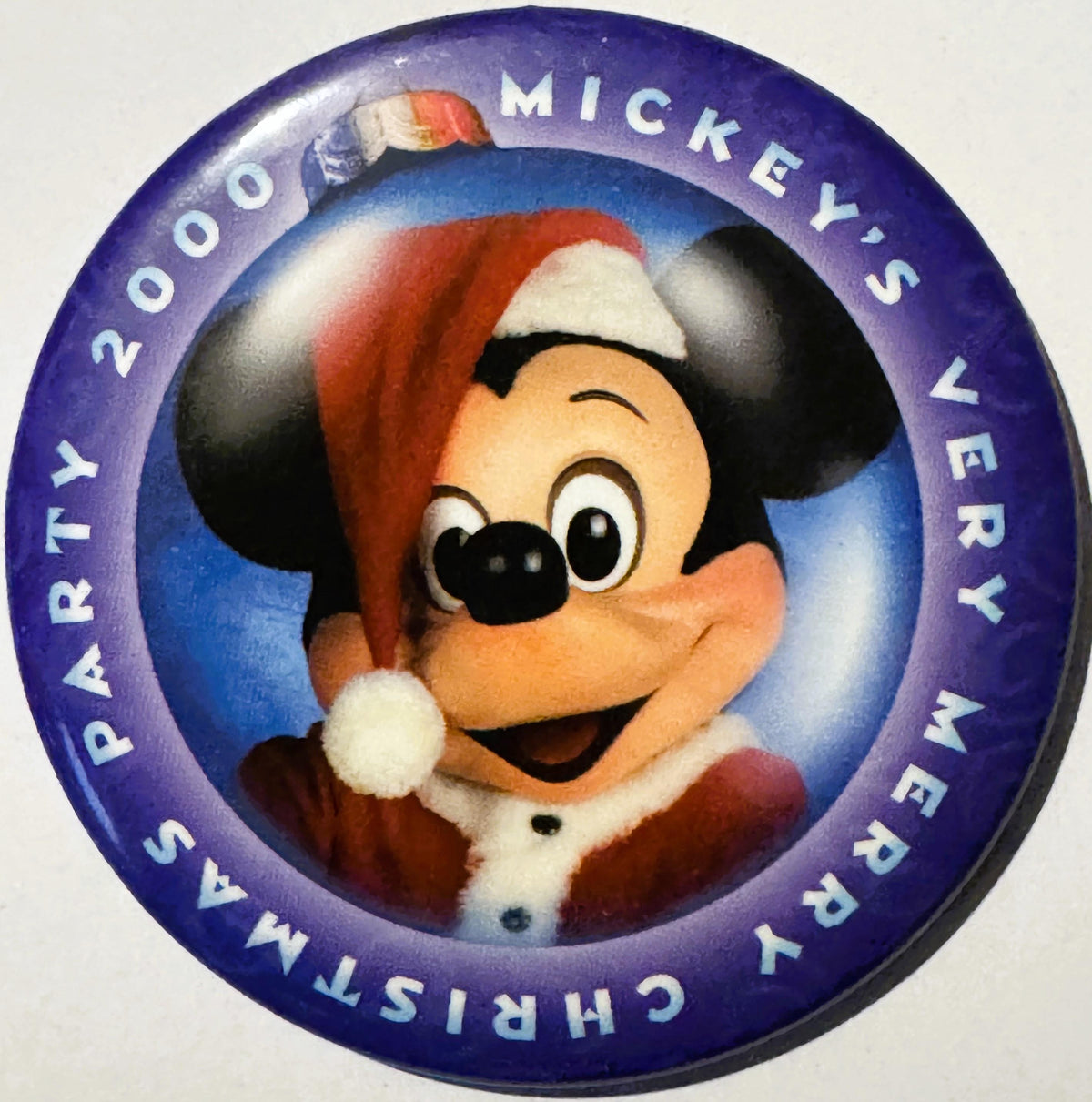 Round purple enamel pin featuring Mickey Mouse in red Santa hat and suit, text reads "Mickey's Very Merry Christmas Party 200