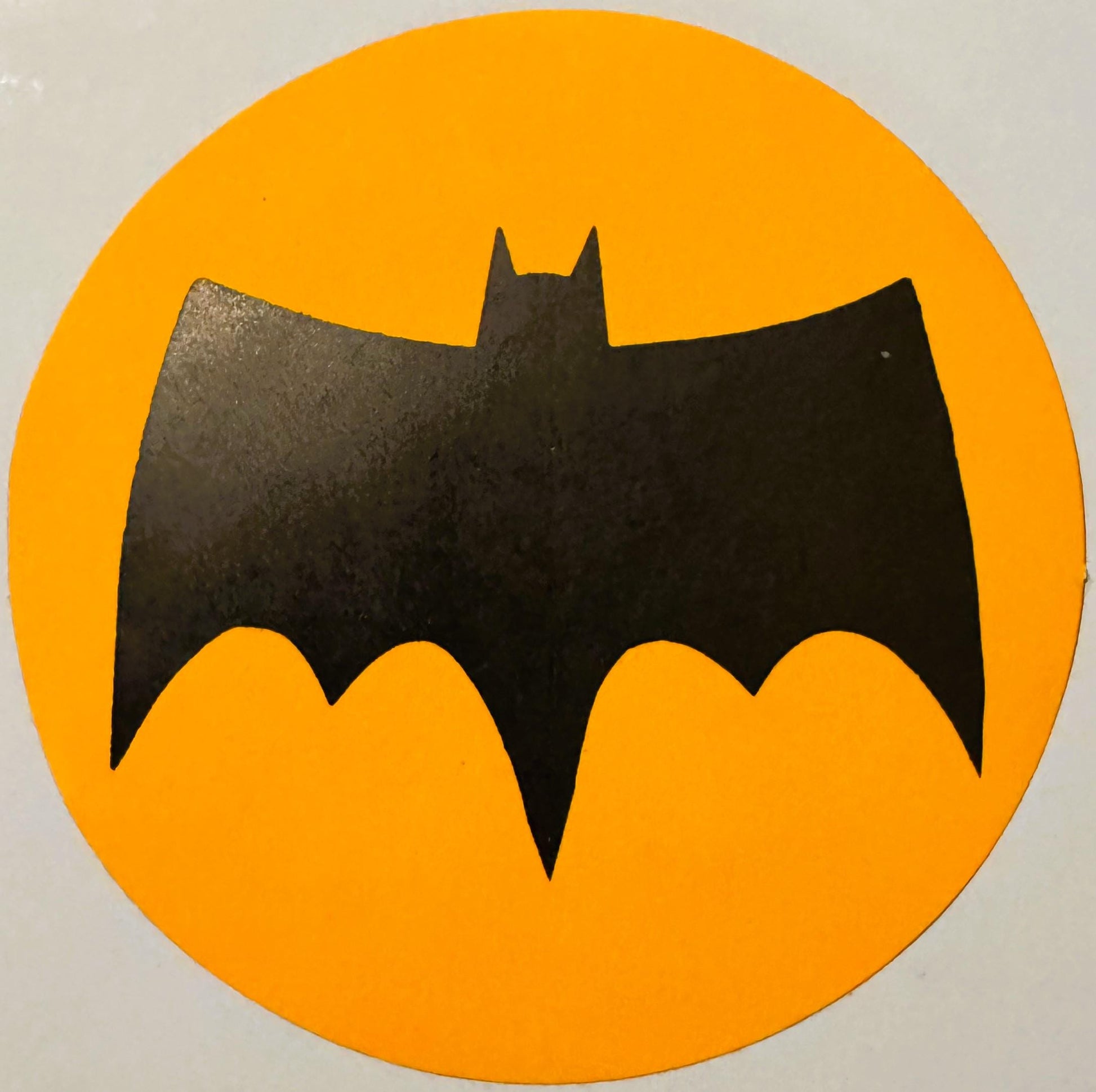 Black bat silhouette with pointed ears on bright yellow circular background, vintage sticker or decal with wear marks visible