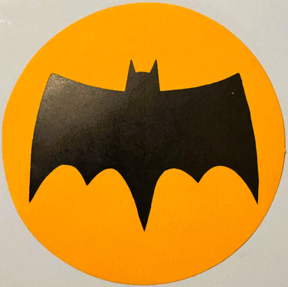 Black bat silhouette with pointed ears on bright yellow circular background, vintage sticker or decal with wear marks visible
