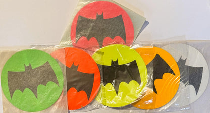 Five Batman signal stickers in original plastic packaging, featuring black bat silhouettes on red, green, orange, yellow, and