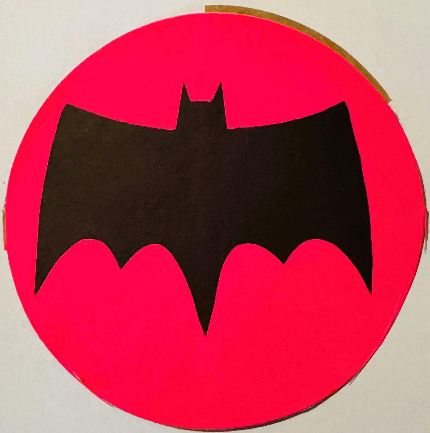 Black bat silhouette on bright pink circular background, vintage sticker or decal viewed flat against white surface