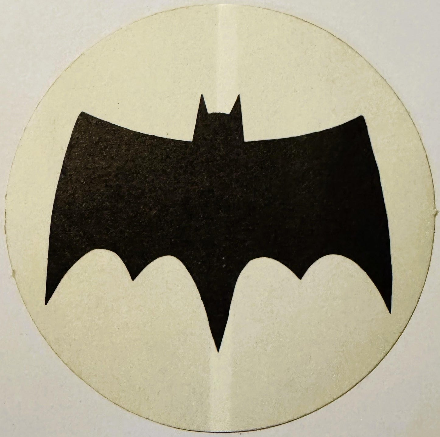Black bat silhouette with pointed ears on cream circular background, vintage sticker or decal