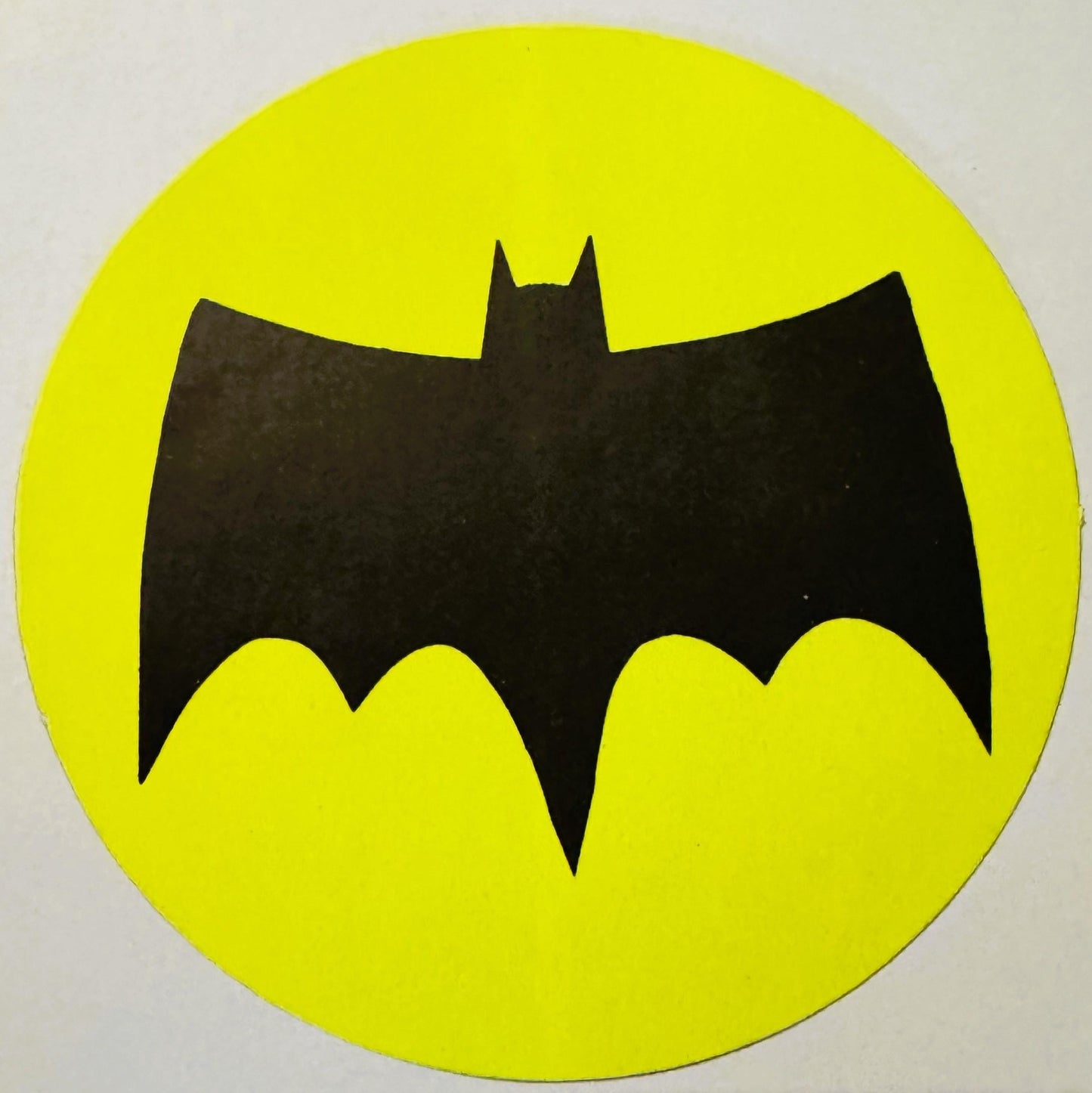 Black bat silhouette with pointed ears on bright yellow circular background, vintage sticker or decal