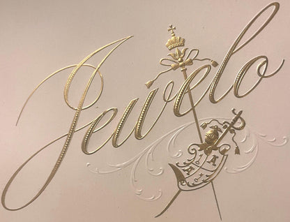 Gold embossed cigar label with "Jewelo" script text, crown and sword emblem, and ornamental flourishes on cream background