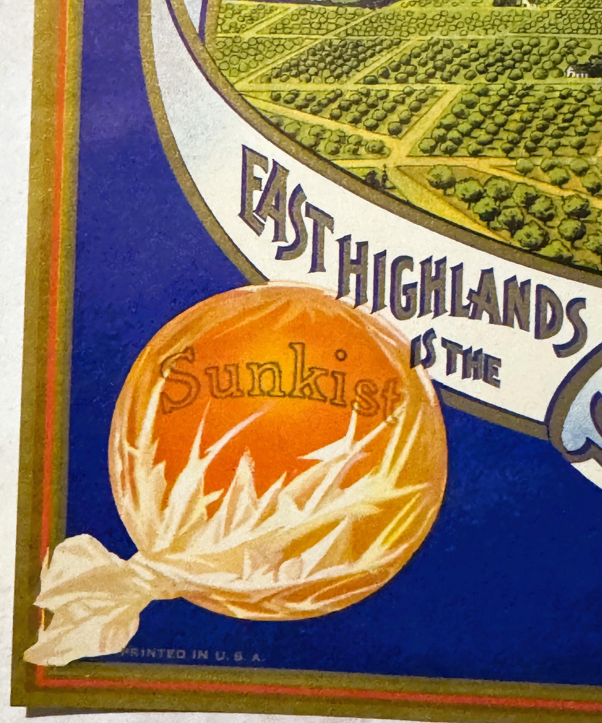 Vintage fruit crate label showing orange with "Sunkist" text, agricultural fields above, blue background, printed in USA, par